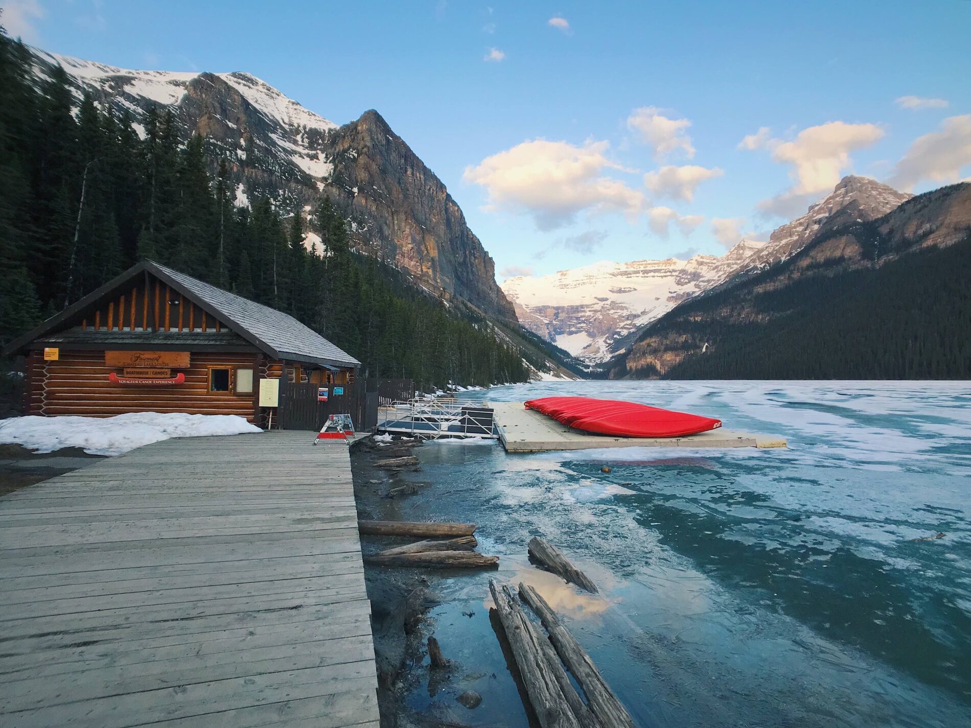 The Lake Louise lakeshore with a log boathouse and red canoes below snowy peaks